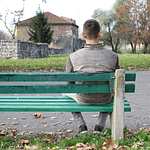 Man, sitting on a park bench alone, facing away from the camera
