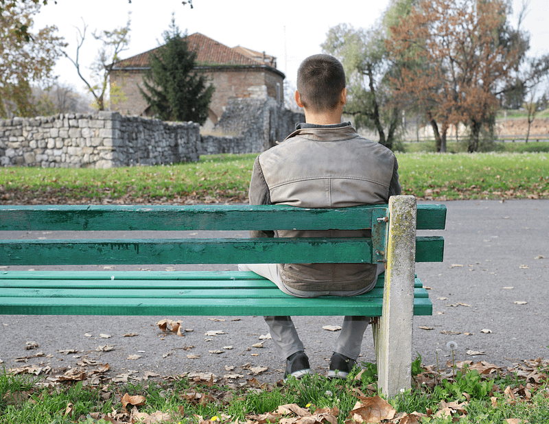 Man, sitting on a park bench alone, facing away from the camera